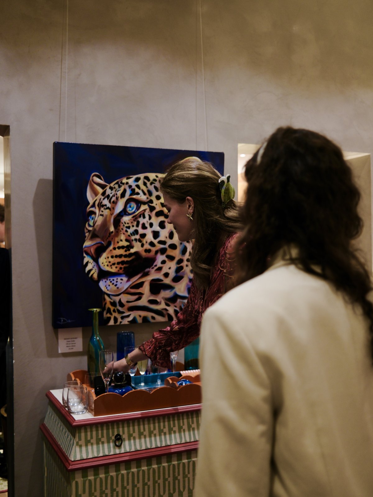 Inside the exhibition, a guest at a drinks table in front of a leopard painting